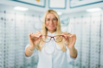 Female optician shows glasses in optics store. Selection of eyeglasses with professional optometrist