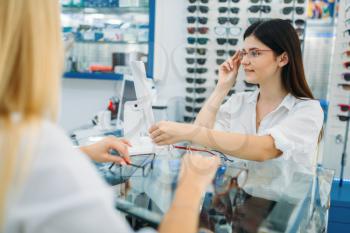 Female optician and consumer chooses glasses frame in optics store. Selection of spectacles