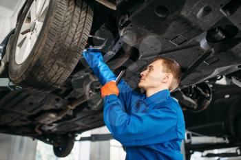 Mechanic with lamp checks car brake hoses, repair station. Tire service, vehicle maintenance