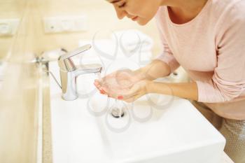 Young woman washes her face at the sink in bathroom. Female person cares for skin. Morning facial cleaning procedure