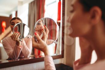 Young woman doing makeup in front of the mirror in the bedroom. Female person cares for skin. Morning face hygiene