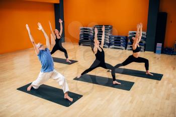 Yoga training class, female group with male instructor in action in gym. Yogi exercise indoor