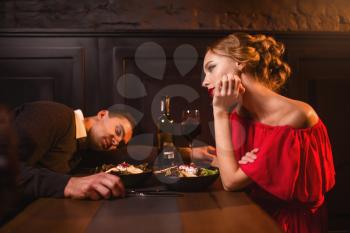 Drunk man sleeps at the table against woman in red dress in restaurant. Couple have a spoiled evening