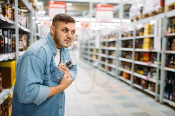 Man hides a bottle of alcohol under his shirt in supermarket. Male thief in shop, husband conducting a covert operation, family shopping
