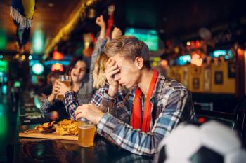 Upset football fan sitting at the counter in sports bar. Tv broadcasting, favorite team loss, game over