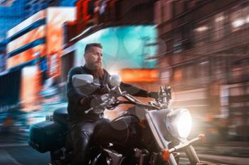 Biker riding on chopper through the night city, blured cityscape and advertising with neon lights on background. Vintage bike, rider on motorcycle, asphalt road adventure, freedom lifestyle