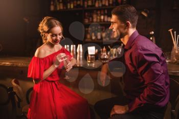 Date in nightclub, attractive woman in red dress flirts with man against bar counter in nightclub. Love relationship, night lifestyle