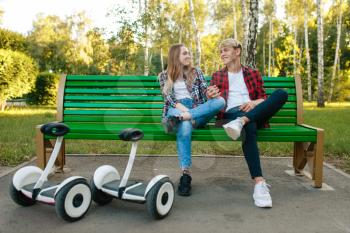Young couple with gyroboard sitting on the bench in park. Outdoor recreation with electric gyro board. Transport with balance technology