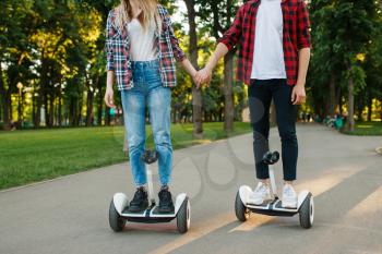 Male and female person riding on gyro board in park. Outdoor recreation with electric gyroboard. Transport with balance technology