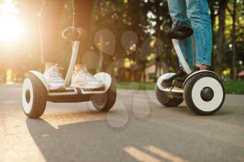 Male and female person riding on gyro board in park at sunset. Outdoor recreation with electric gyroboard. Transport with balance technology, gyroscope