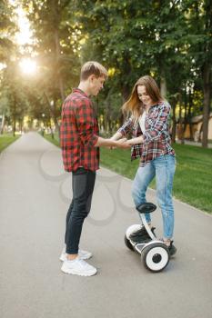 Boyfriend teaches his girl to ride on gyro board in summer park. Outdoor recreation with electric gyroboard. Transport with balance technology