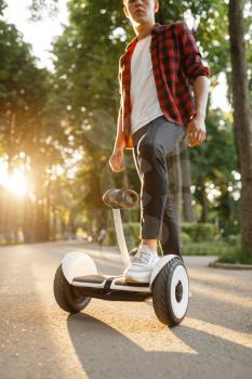 Young male person riding on gyroboard in summer park. Outdoor recreation with electric gyro board. Eco transport. Electrical gyroscope vehicle