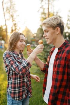 Young love couple feed each other ice cream in summer park. Boyfriend and girlfriend leisures together with ice-cream, romantic walk
