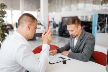 Manager and buyer make out the purchase of new car in showroom. Male customer buying vehicle in dealership, automobile sale