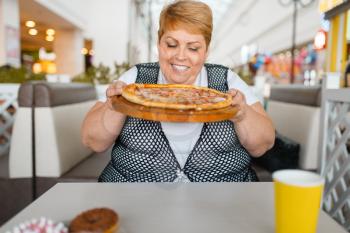 Fat woman eating pizza in fastfood restaurant, unhealthy food. Overweight female person at the table with junk dinner, obesity problem