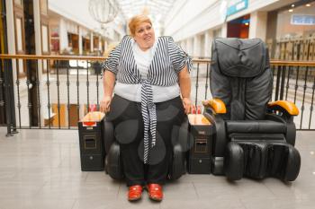Fat woman is not placed in a massage chair in mall. Overweight female person tries to sit in a leather armchair in supermarket, obesity problem