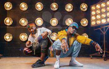 Two black rappers sitting on the floor, perfomance on stage with spotlights on background. Rap performers on scene with lights, underground music, urban style