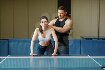 Man doing massage to woman, ping pong training indoors. Couple in sportswear holds rackets and plays table tennis in gym