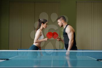 Man and woman on ping pong training indoors. Couple in sportswear holds rackets and plays table tennis in gym. Male and female persons in table-tennis club