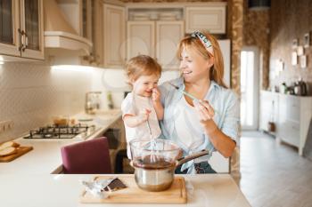 Young mother with her daughter mixing melted chocolate in a bowl. Cute woman and little girl cooking on the kitchen. Happy family prepares sweet dessert