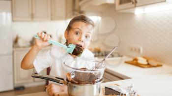 Young boy tastes melted chocolate in a bowl. Kid cooking on the kitchen. Happy child prepares a dessert