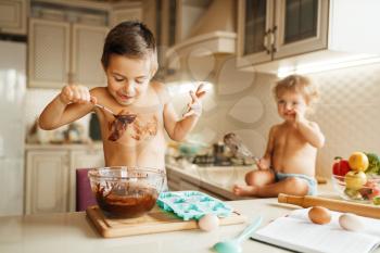Little kids tastes melted chocolate. Cute boy and girl cooking on the kitchen. Happy children prepares sweet dessert at the table