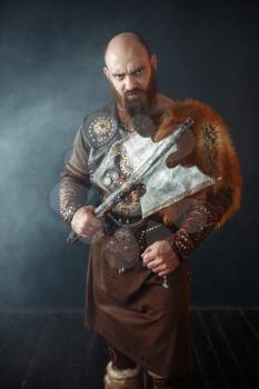Bearded viking with axe enters the battle, barbarian image. Ancient warrior in smoke on dark background