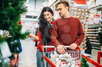 Couple buying christmas tree in supermarket. December shopping, choosing of holiday decorations