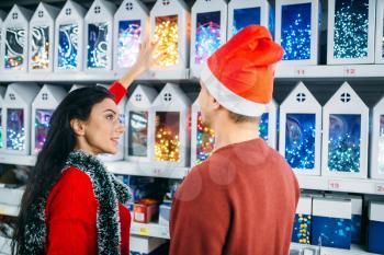 Young couple looks on christmas gifts in supermarket, family tradition. December shopping, choosing of holiday decorations