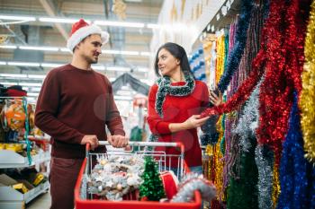 Young couple in the department of holiday decorations in supermarket, family tradition. December shopping