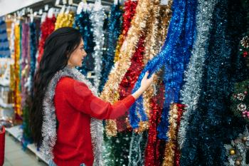Young woman choosing holiday fluffy garland, purchase of christmas decoration in supermarket, family tradition. December shopping