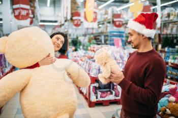 Young couple choosing plush toys on christmas in supermarket, family tradition. December shopping of new year holiday goods and decorations