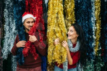 Young couple plays with holiday fluffy garland, purchase of christmas decoration in supermarket, family tradition. December shopping