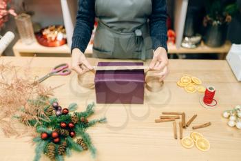 Female seller decorates gift box with wrapping paper and golden ribbon, decoration process. Woman wraps present on the table, decor procedure