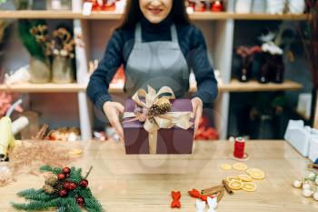 Female seller shows christmas gift box with handmade wrapping. Woman wraps present on the table, festive decor