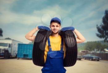 Serviceman in uniform holds tires in hands. Repairman, wheel mounting, tyre service
