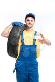 Tyre service, worker in blue uniform holds tire and empty businesscard in hands, white background, repairman, wheel mounting