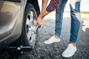 Male person hands with wheel wrench, broken car. Vehicle with puncture tire on roadside