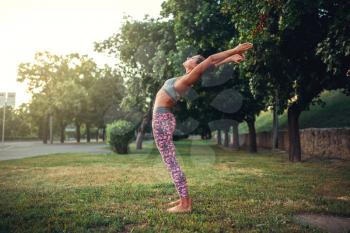 Woman doing yoga exercise on the grass in summer park. Morning yogi meditation