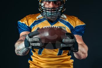 American football player with laced ball in hands, black background. Contact sport