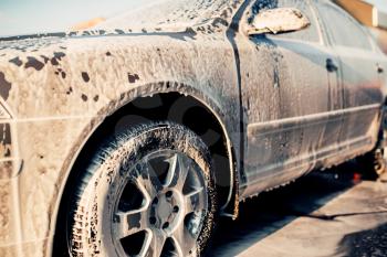 Wet vehicle in foam, automobile in suds, car wash. Carwash station