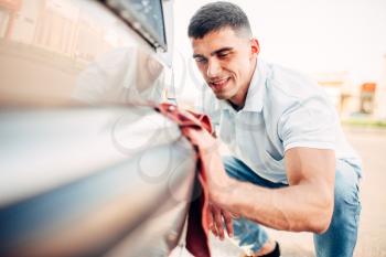 Car exterior polishing on carwash station. Man rubbing vehicle bumper with automobile polish