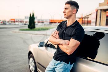 Smiling man standing near his car outdoors, advertising concept. Automobile lifestyle. Auto business