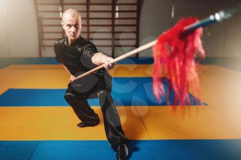 Wushu master training with spear, martial arts. Man in black cloth poses with blade