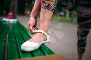 Sporty female person buttons footwear, sport bottle and towel on the bench on background. Woman in sportswear on fitness training