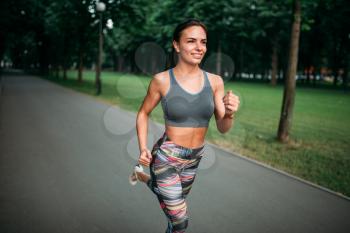Slim woman jogging on sidewalk in summer park. Female runner on outdoors morning workout