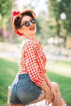 Sexy pinup girl in denim shorts and sunglasses outdoors, retro american fashion. Attractive woman in pin up style