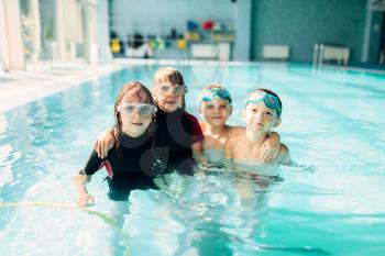 Portrait of friendly children with swimming goggles in pool. Healthy and happy childhood concept. Funny children in swimming pool.Boys and girls in clean blue water.