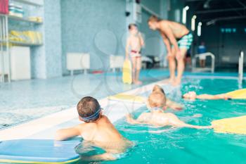 Swimming sports activity. Children swimming in pool. Healthy and happy childhood concept. Kids in water with planks for swimming. Instructor talking to child on background.