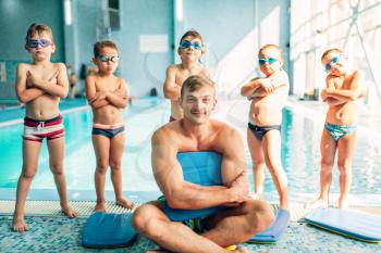 Portrait of male instructor with children near swimming pool. Cute boys with swimming goggles stands near water. Healthy and happy childhood concept.